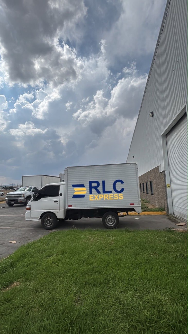 Unidad de caja blanca rotulada con el logo de RLC Express estacionada frente a una nave industrial en San Luis Potosí